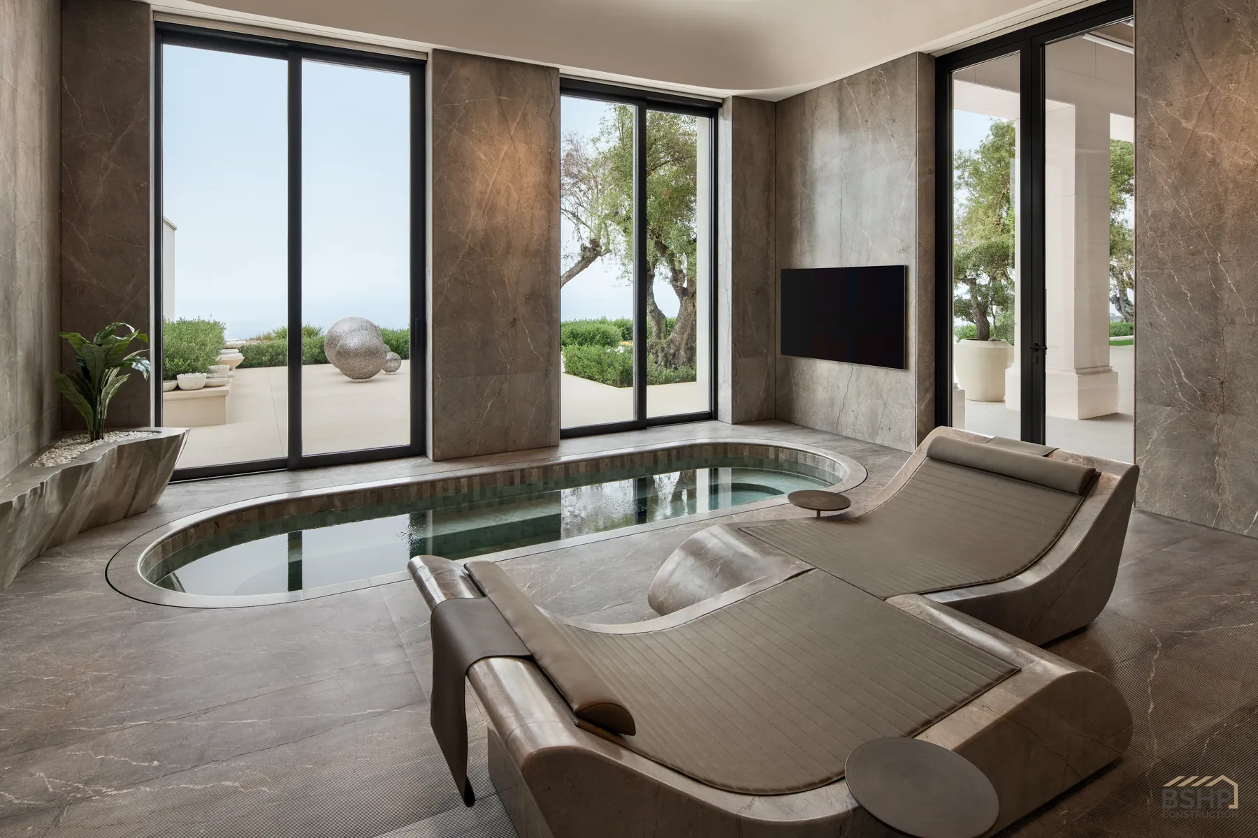 Indoor spa pool and stone chaise loungers framed by floor-to-ceiling glazing
