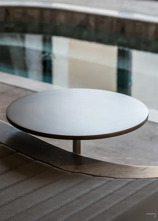 Round bronze table on the ribbed stone pool deck