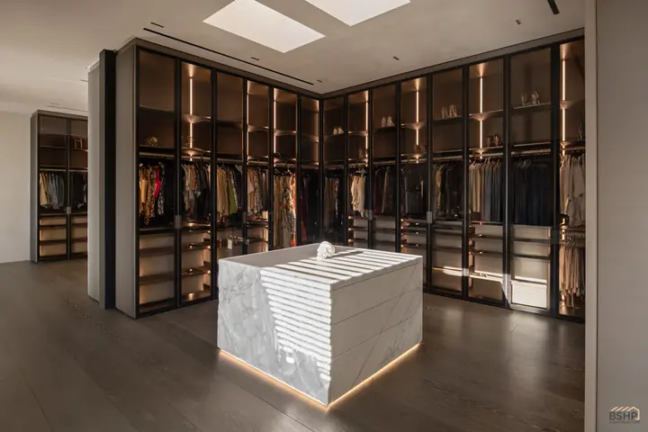 Glass-front wardrobes and carved marble island beneath a skylight in the dressing suite